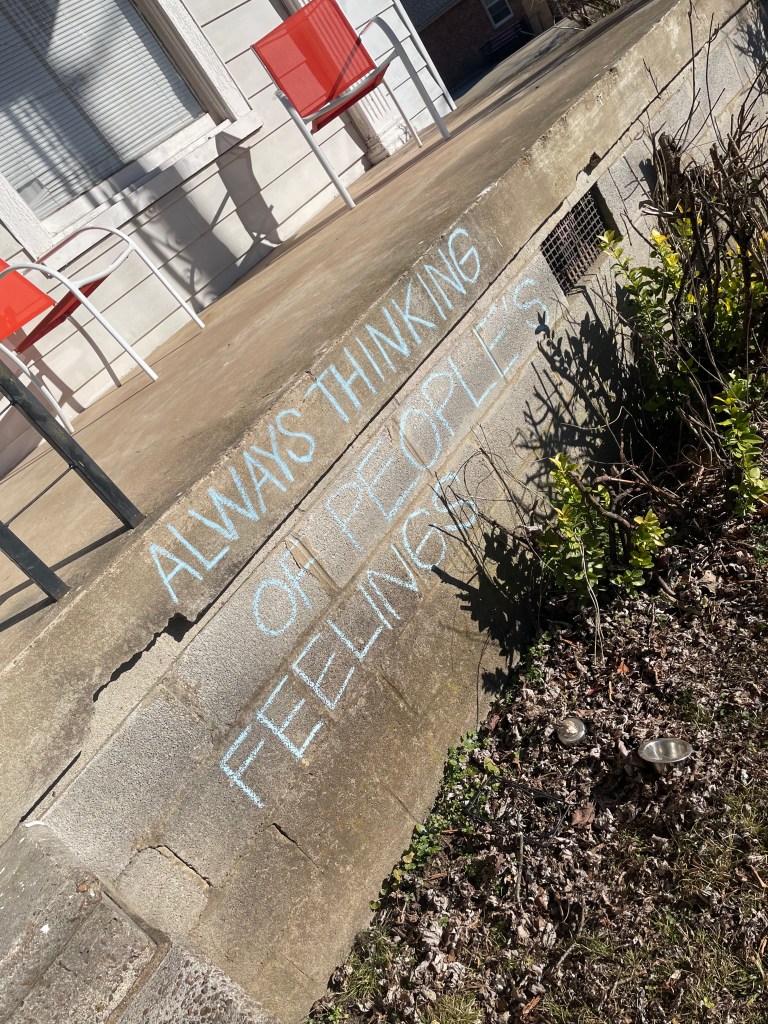 chalk graffiti on a front porch in East Nashville. the chalk is light blue and it says ALWAYS THINKING OF OTHER PEOPLE'S FEELINGS